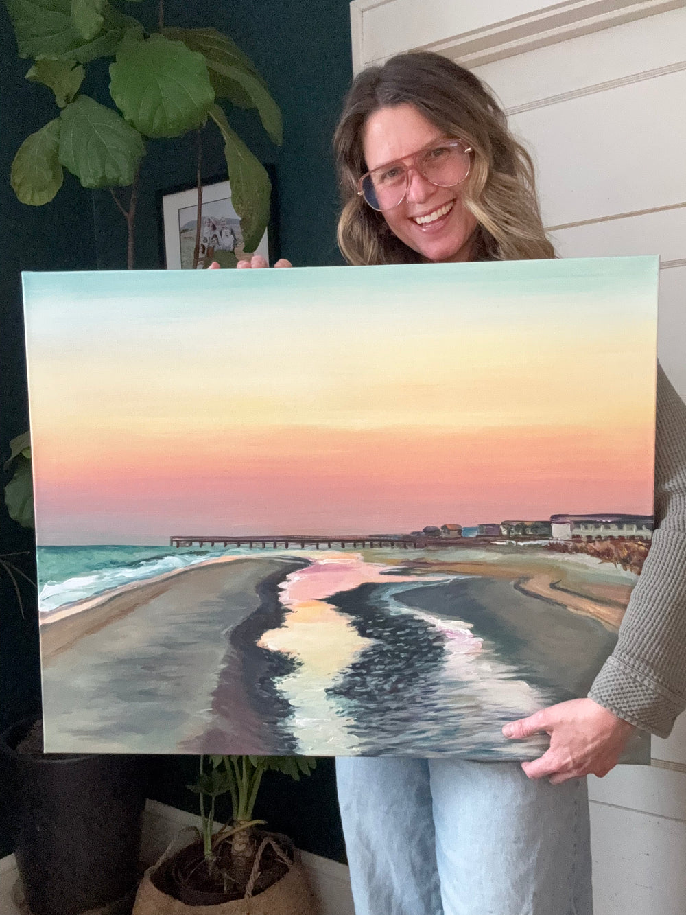 Person holding a painting of a beach scene with a sunset.